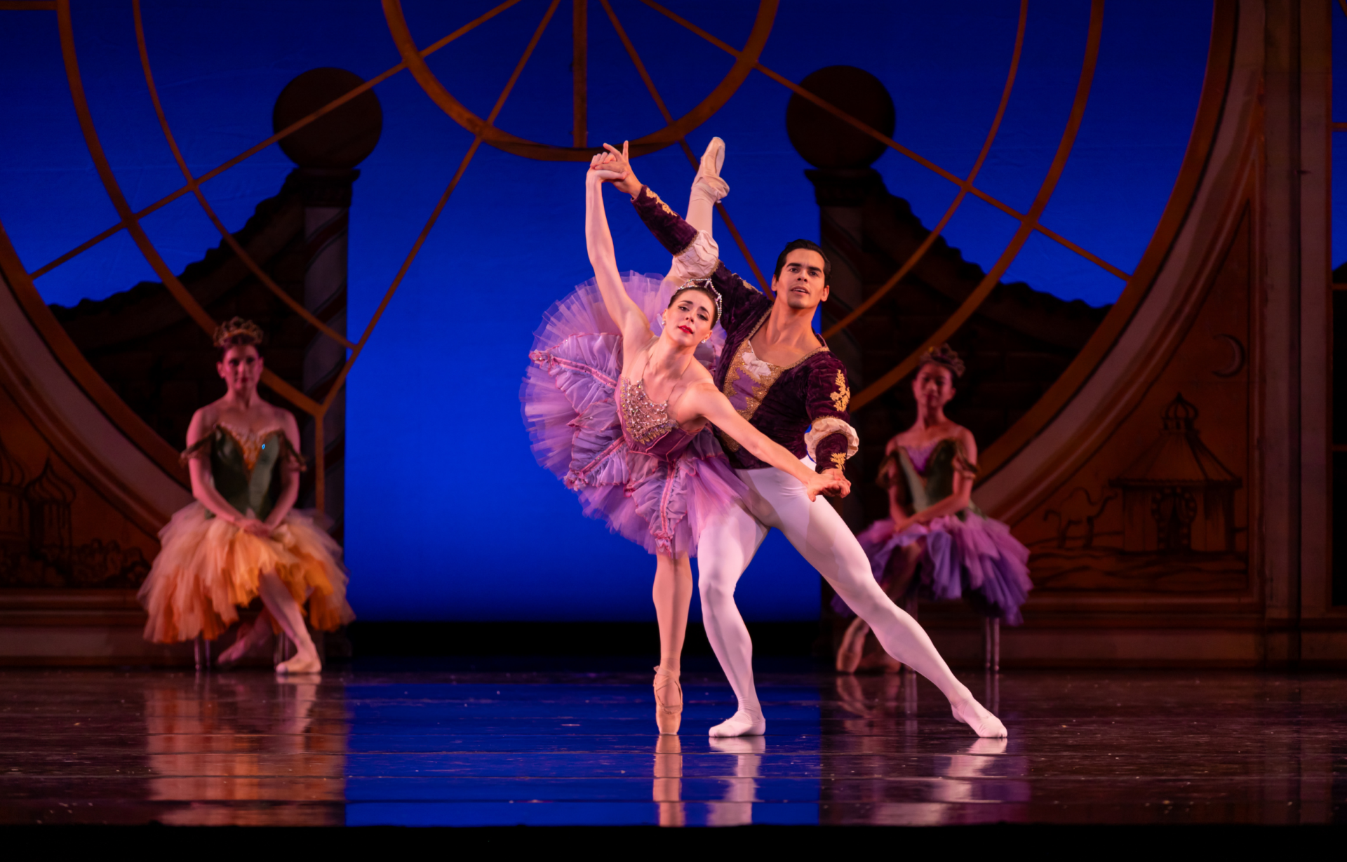 The Sugarplum Fairy, in a vibrant and ornate purple costume, dances with her cavalier in The Nutcracker.
