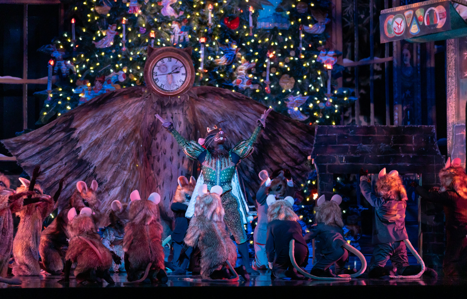 The Mouse King celebrates with his minions on stage in The Nutcracker. There is a large clock and Christmas tree behind him.