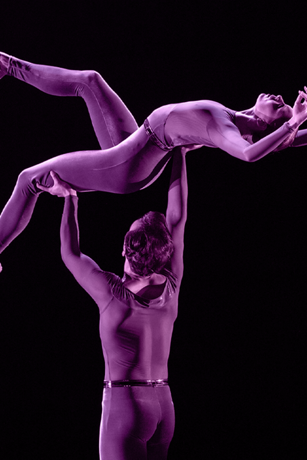 Man is holding up a fellow dancer in a graceful pose. There is a purple effect on the entire image.