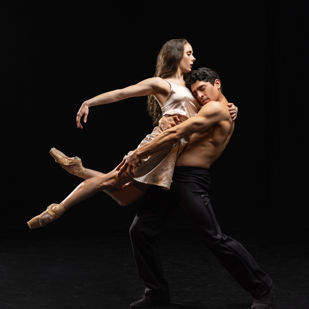 BalletMet dancers in an intricate pose at a promotional shoot for La Bohème. The female dancer is in a champagne-colored silk dress and point shoes while the male dancer is in just black pants.
