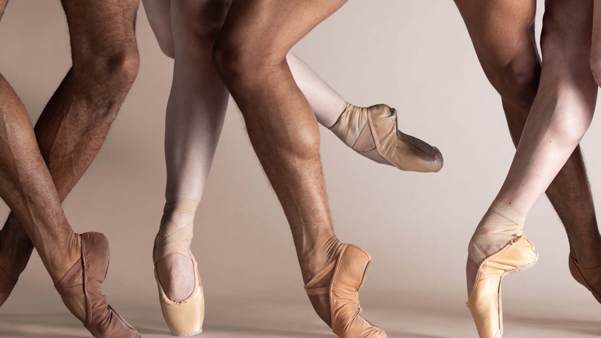 Ballet dancers’ legs in various skin-toned pointe shoes, posed gracefully against a neutral background.
